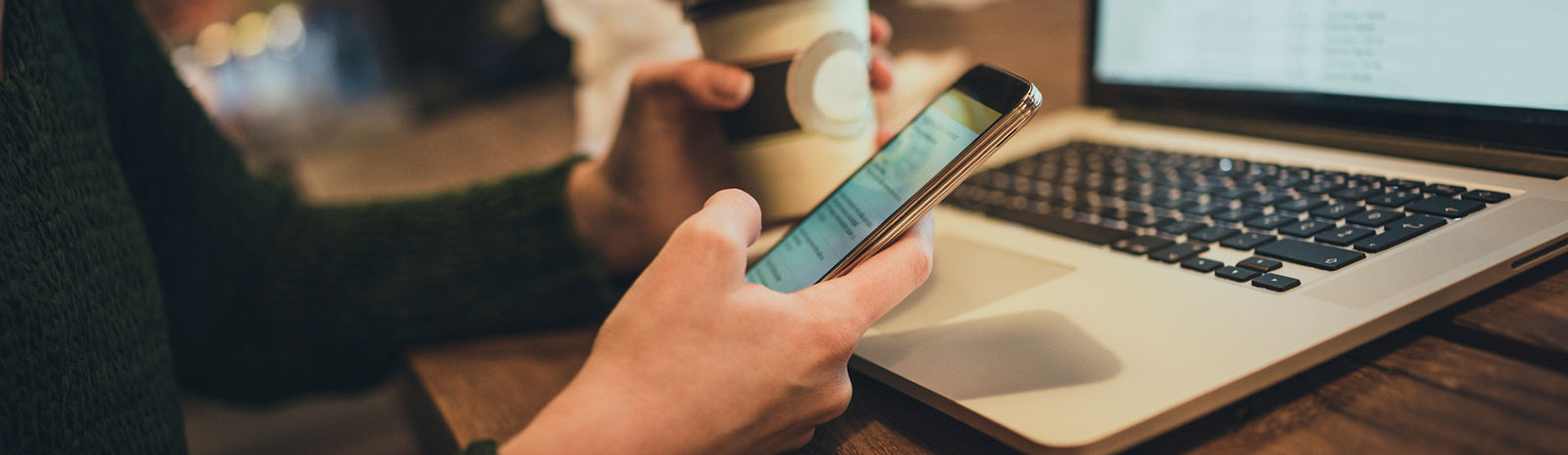 person holding mobile phone and looking at laptop